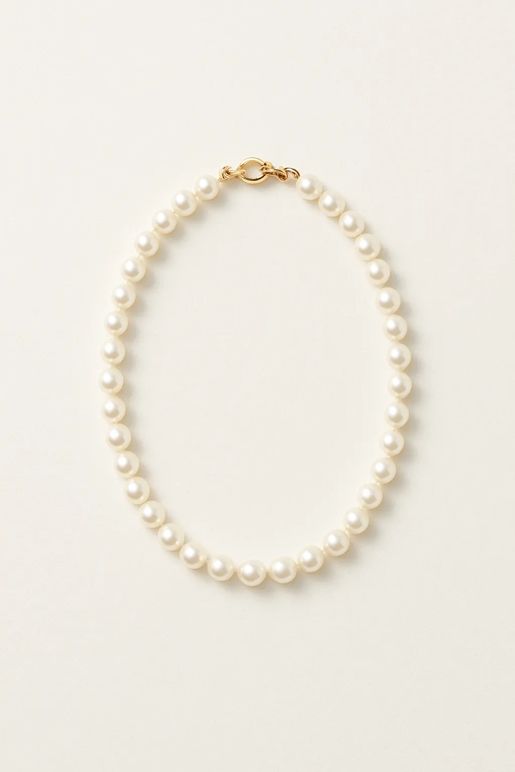 Elegant pearl pendant necklace with a delicate gold chain on a person wearing a white garment with soft beige background, no human shapes visible