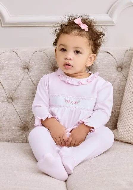 Baby wearing pink floral pajamas or outfit sitting on a neutral background. Cute children's sleepwear design.