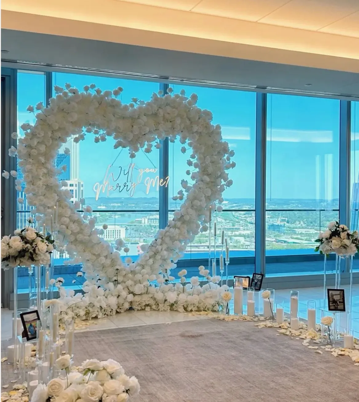 Elegant proposal setup with heart-shaped flower arch, neon sign, and multiple floral arrangements. No human shapes.