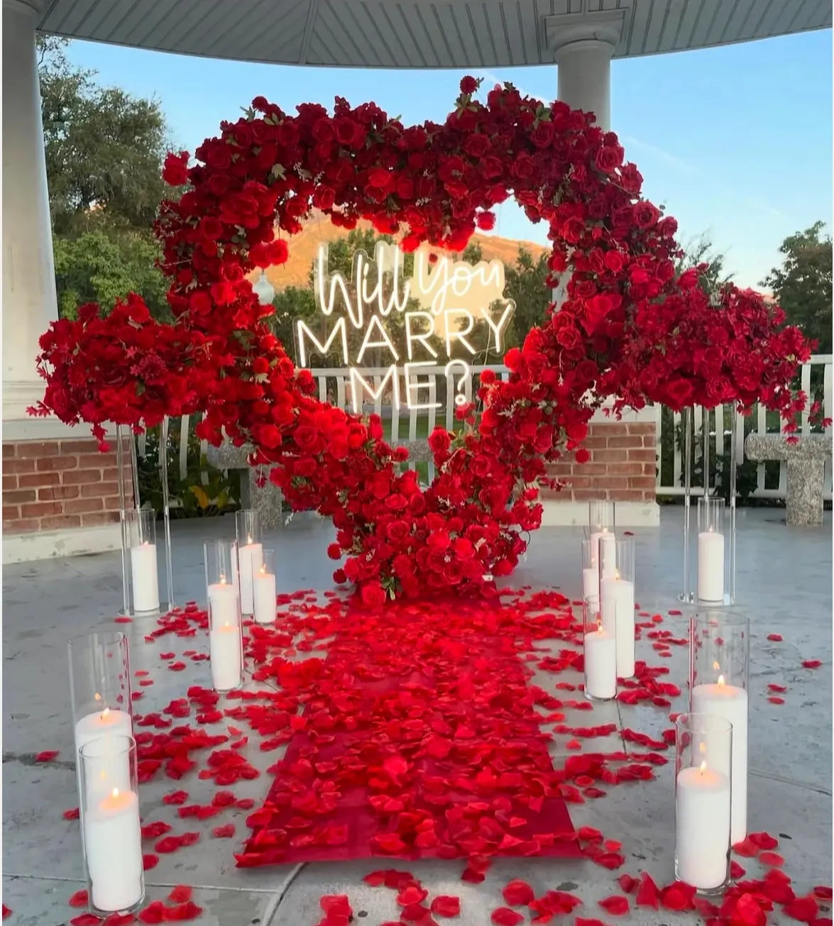 Intimate proposal setup with heart-shaped flower arch, neon sign, and romantic decorations. No human shapes.