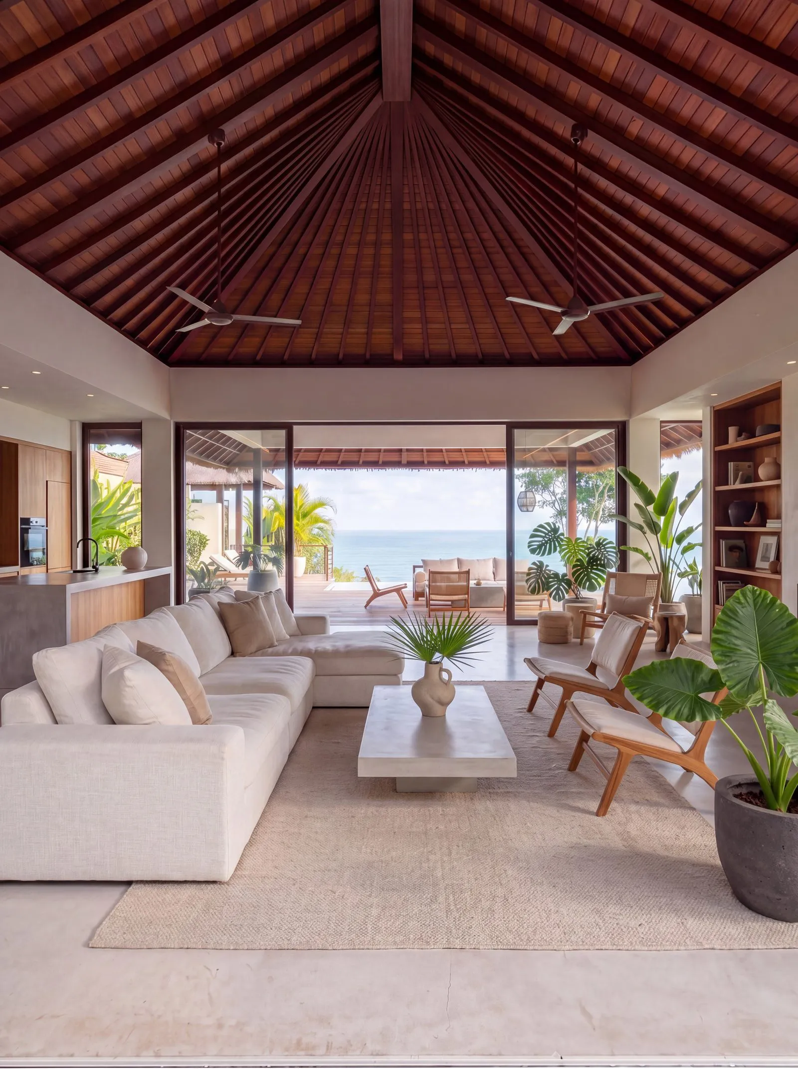 Wide shot of a fully styled great room with white sectional, teak coffee table, ocean view
