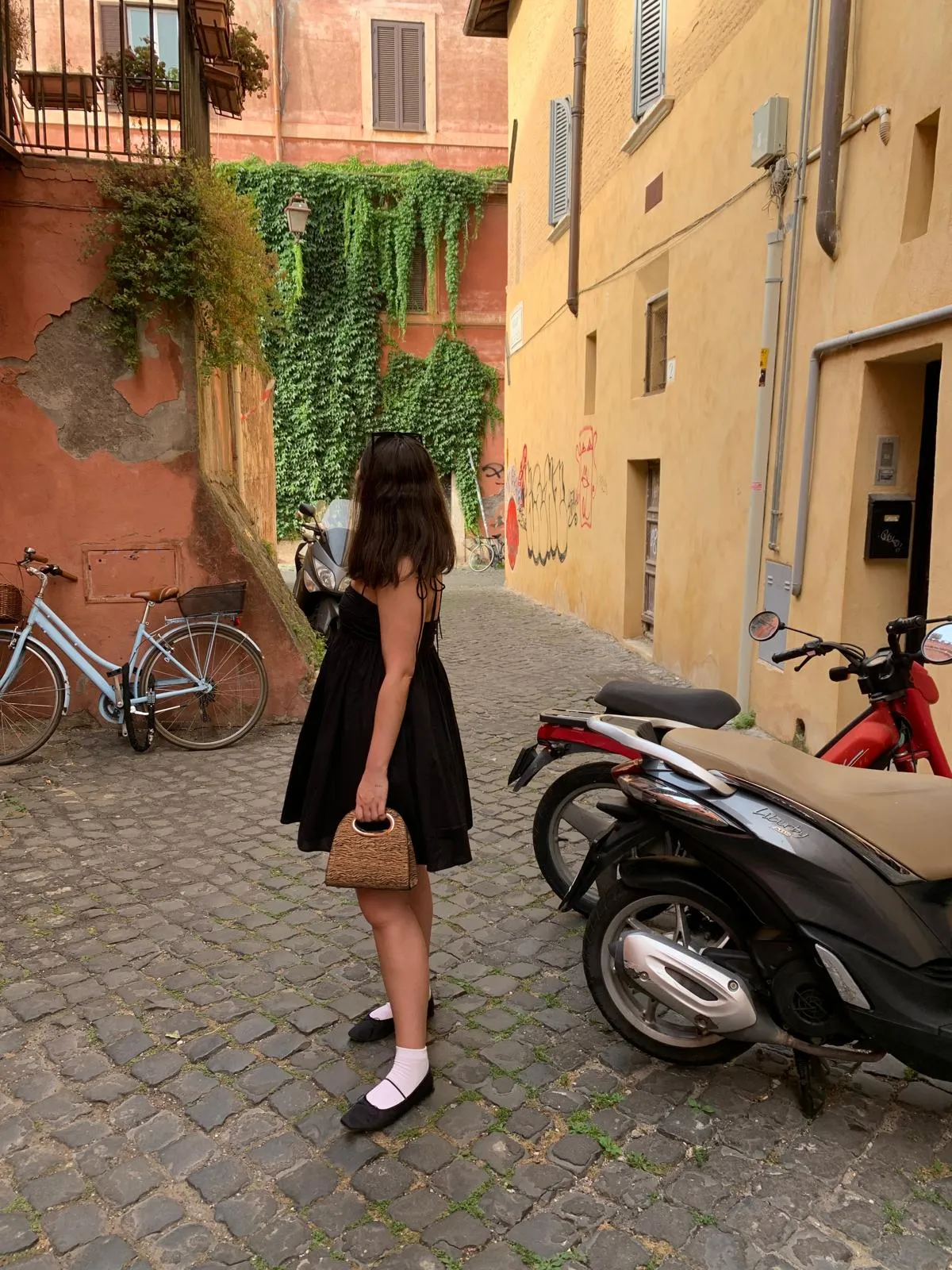 A cobblestone street in Italy with rustic terracotta and yellow buildings covered in ivy, featuring vintage bicycles and scooters parked along the narrow alleyway. No human shapes should be included.