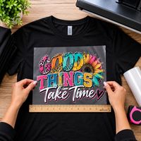 Hands positioning a colorful DTF transfer on a black T-shirt with a ruler used to check the design width.