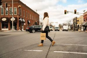 Woman crossing street with Neighbors bag