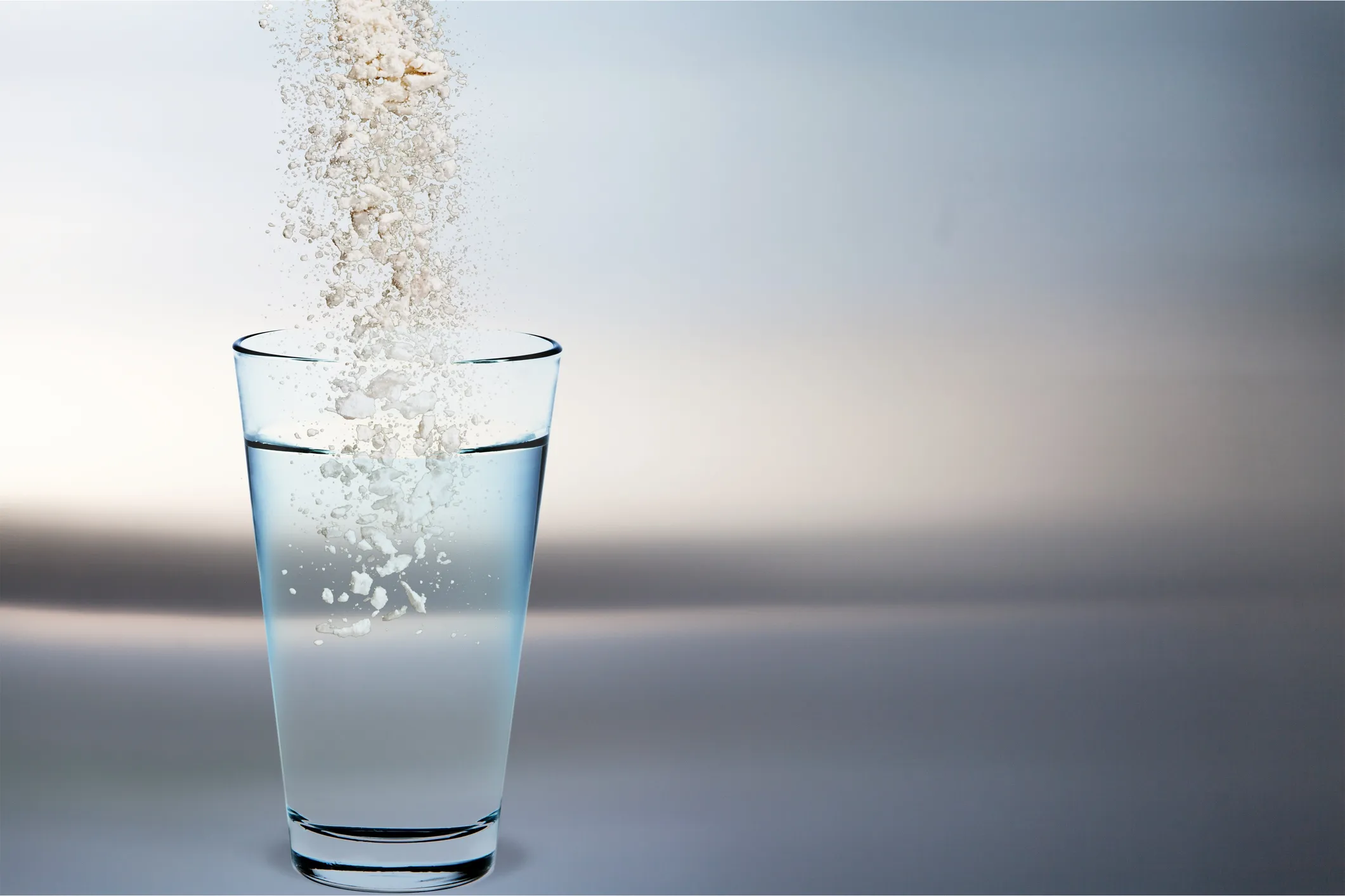 Natural spring water flowing over ceramic conversion materials, with vibrant minerals being added back to purified water. Crystal clear water with a slight blue hue showing mineral content. No human shapes.