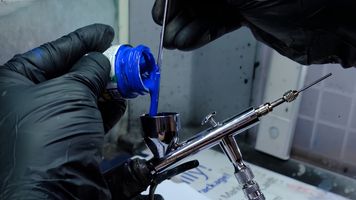 Pouring paint into an airbrush using a stir stick for neatness.