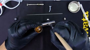 Cleaning an airbrush with cleaner and a brush.