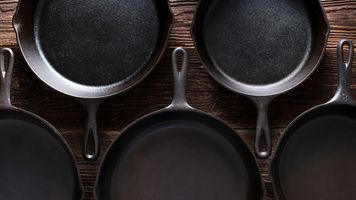Five cast iron skillets on wood table.
