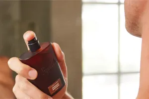 Man spraying himself with bottle of cologne.