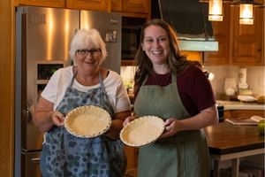 Two women holding pie pans containing pie crusts.