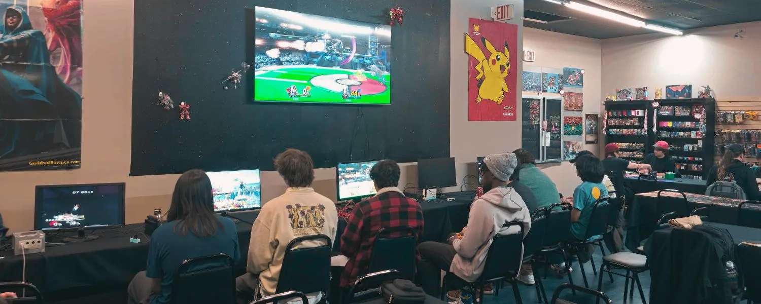 People playing video games at TOTL Games, Portland's queer game store, with a large screen showing a tournament match and game shelves in the background