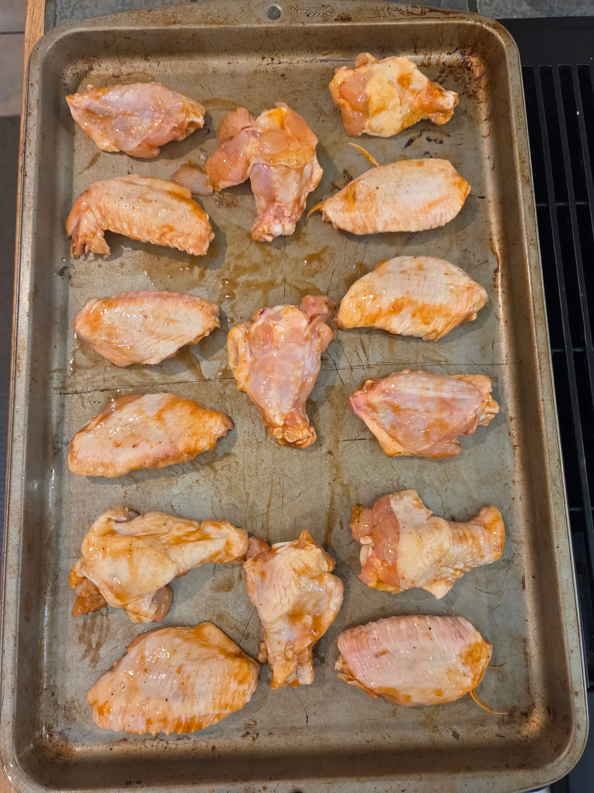 Sauce-coated wings arranged neatly on a foil-lined baking sheet ready to go into the oven, showing the bright red color of the buffalo sauce, no human shapes